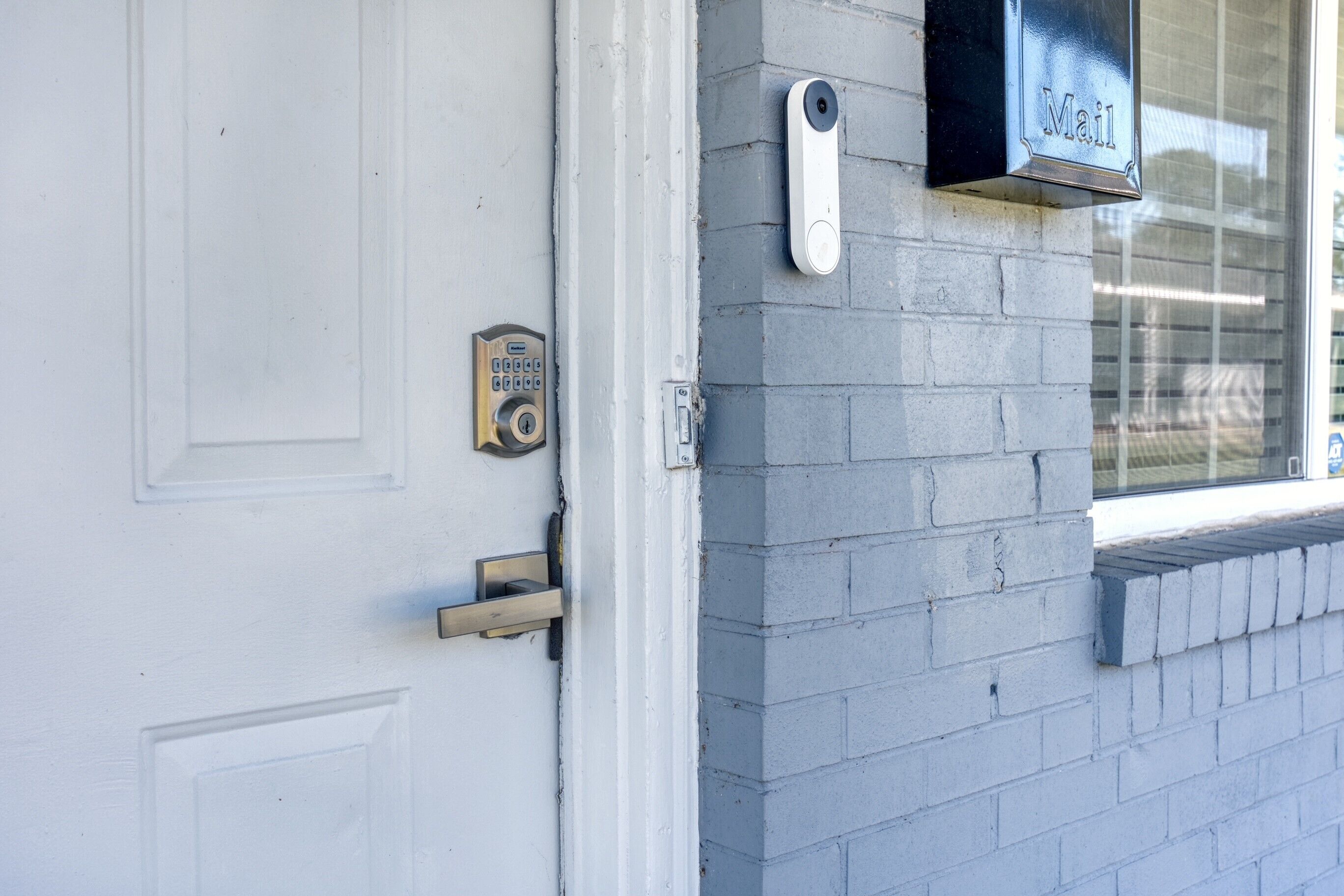 A white door with a keypad lock, a mail slot, and a mailbox on a gray brick wall.