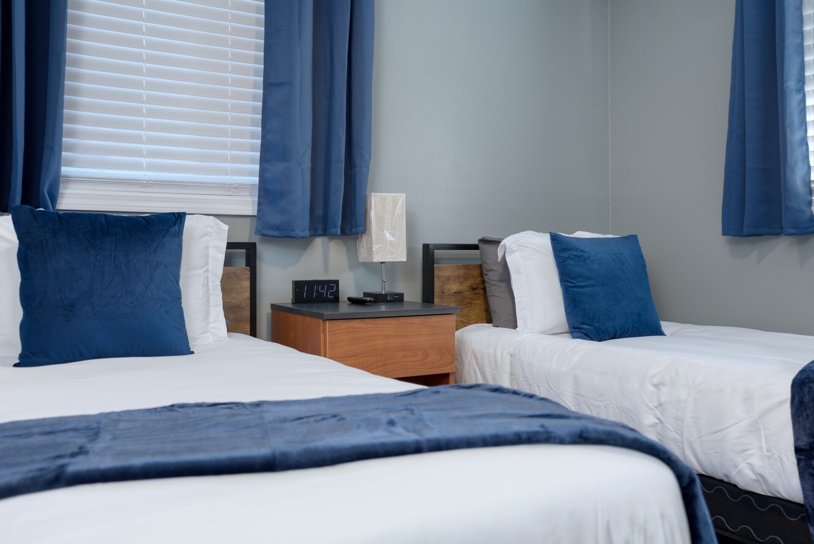 Een hotelkamer met twee bedden, een nachtkastje met een klok en een raam met gordijnen.