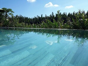 A clear blue pool with a wooden deck, surrounded by lush greenery and palm trees. - Deluxe Twin Room with Garden, Lake View, WiFi (Hoi An)