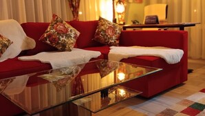 A modern living room with a red sofa, floral cushions, a glass coffee table, and a wooden side table. - Close to BER/Adlershof airport in a quiet location; freeway transportation; (Schönefeld)