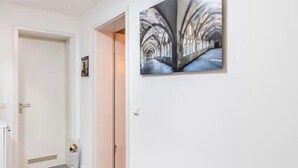 A hallway with a white door, a framed painting of a corridor, and a glass vase with colorful balls. - Close to BER/Adlershof airport in a quiet location; freeway transportation; (Schönefeld)