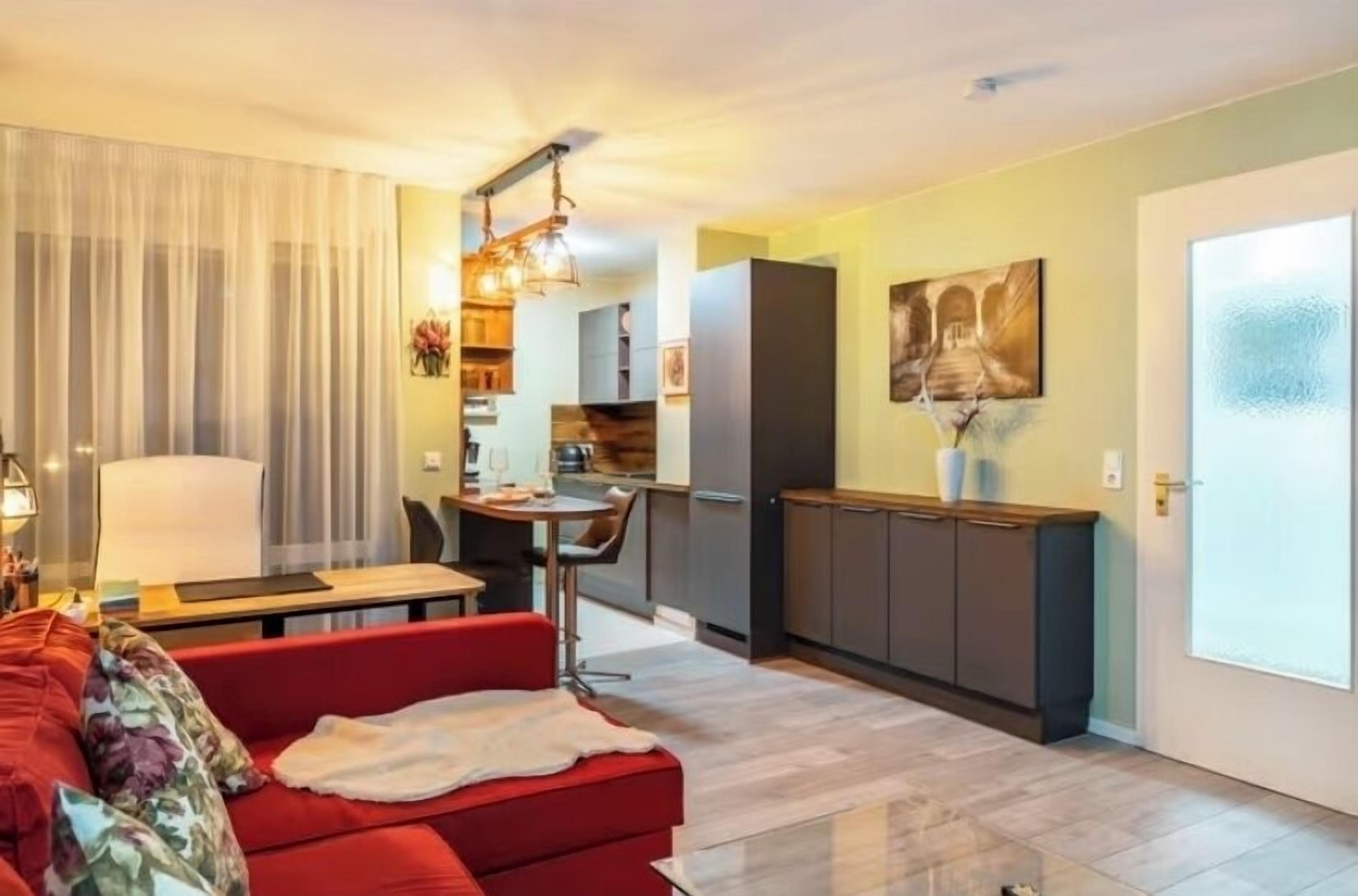 Uma sala de estar moderna com um sofá vermelho, uma área de jantar e uma cozinha.
