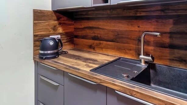 A kitchen with a wooden backsplash, a sink, and a kettle on the countertop. - Close to BER/Adlershof airport in a quiet location; freeway transportation; (Schönefeld)