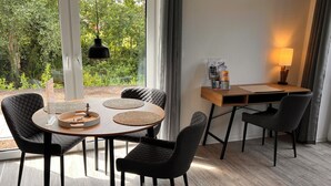 A modern dining area with a round table, four chairs, and a wooden desk with a lamp.