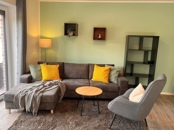 A living room with a sofa, two armchairs, a coffee table, and a rug. There are two wall-mounted shelves with decorative items. - New comfort apartment Nordic at Nature, Emden by Fewo & Zimmer Bruns (Emden)
