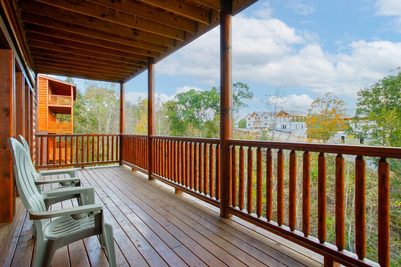 Une terrasse en bois avec une rambarde, un banc et une vue sur une maison et des arbres.