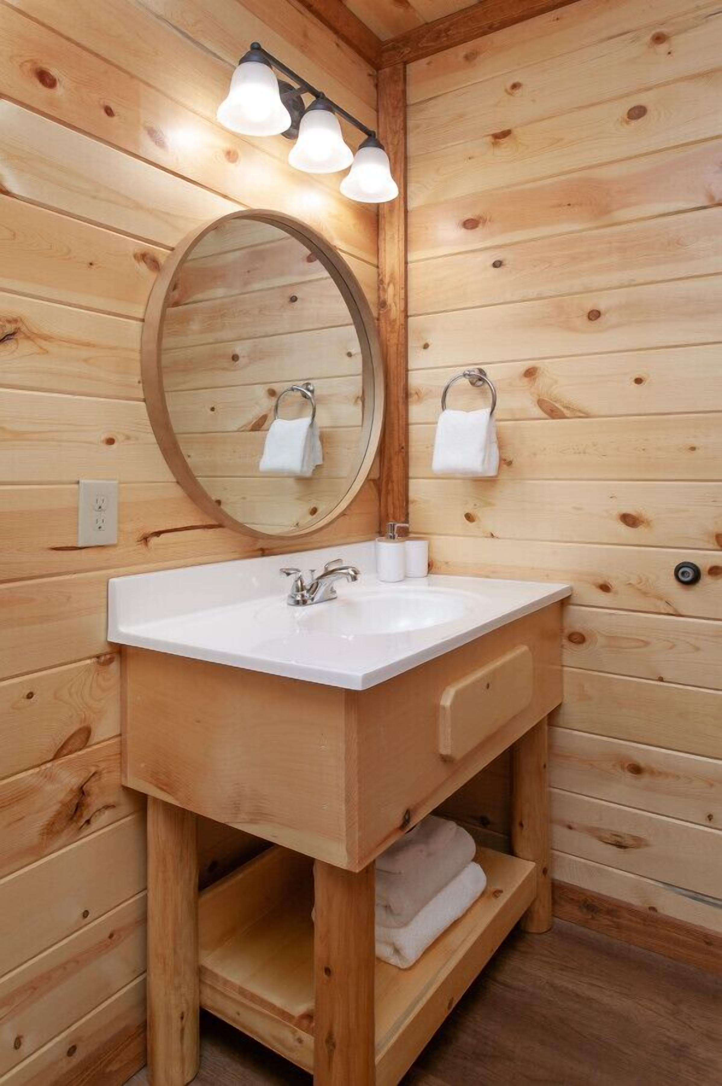 Un baño de cabaña de madera con un lavamanos blanco, un espejo y un perchero para toallas.