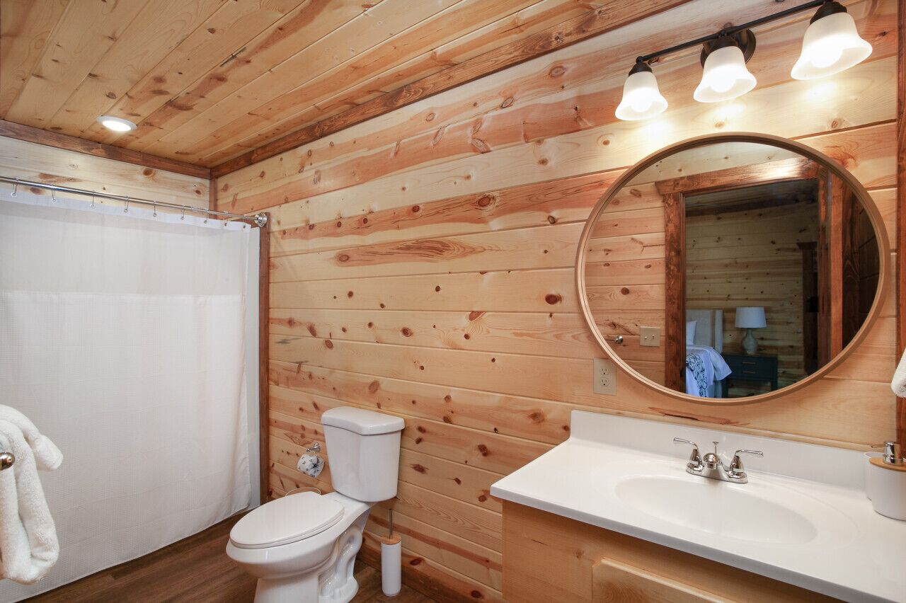 A wooden-paneled bathroom with a toilet, sink, and mirror.