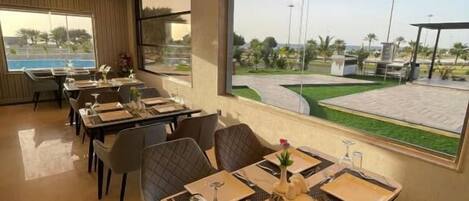 A restaurant with tables set for dining, large windows offering a view of the outdoors, and a modern interior design.