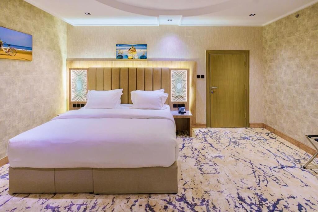A hotel room with a large bed, a wooden headboard, a nightstand, a lamp, and a door.