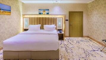 Habitación de hotel con una cama grande, cabecera de madera, mesita de noche, lámpara y una puerta.