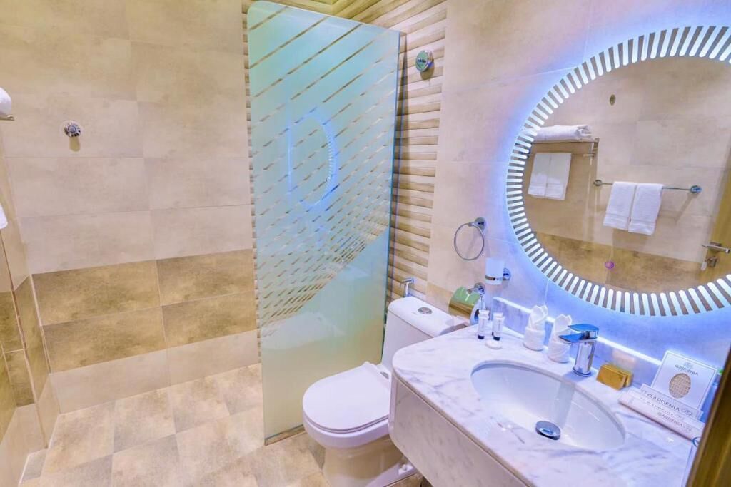 A modern bathroom with a glass shower enclosure, a marble sink, and a large mirror with a circular frame.
