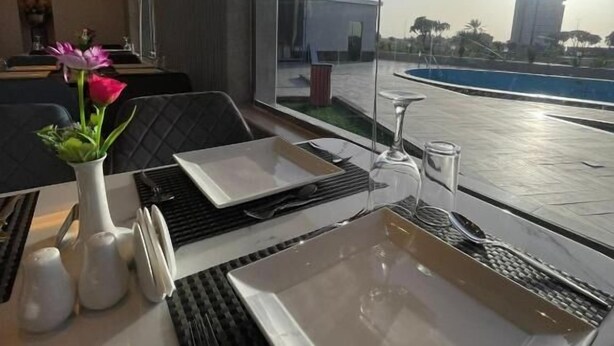 A dining area with a table set for two, a vase with flowers, and a view of the cityscape and water. - Wissam Al Hawraa Hotel (Umluj)
