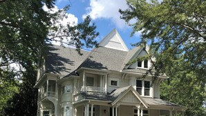 Une grande maison à deux étages, dotée d’une véranda qui fait le tour de la maison, de nombreuses fenêtres et d’un toit à forte pente.
