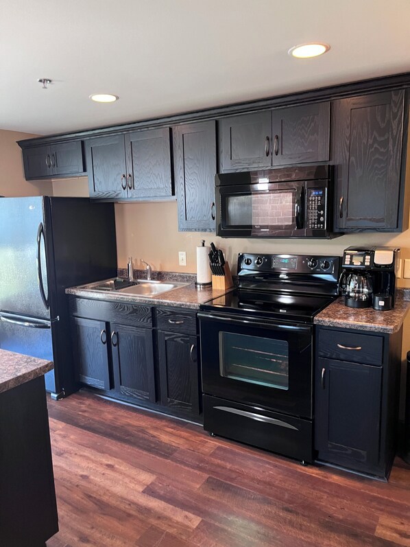 A modern kitchen with dark wood cabinets, a stainless steel refrigerator, a microwave, an oven, and a coffee maker.