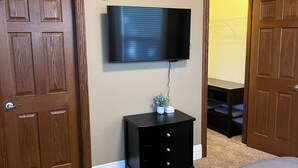 Une chambre à coucher avec un grand lit, un téléviseur à écran plat fixé au mur, une table de chevet en bois et deux portes.