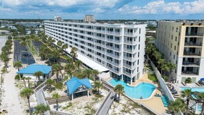 A hotel with multiple floors, a swimming pool, and a beach area with palm trees. - Gulf View Island 2/2 Condo w/ Restaurant Nearby (Fort Walton Beach)