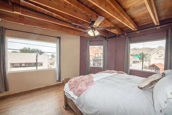 Une chambre avec un plafond en bois, un lit avec une literie blanche, un plaid rose et un ventilateur de plafond.