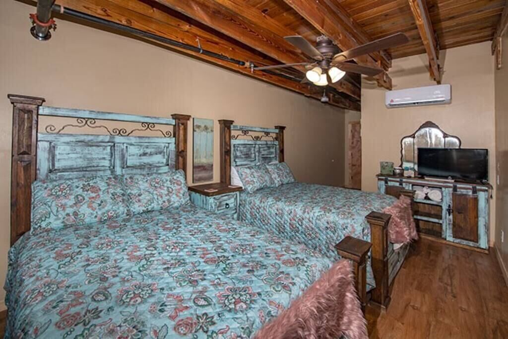 A bedroom with a large bed, a ceiling fan, a TV, and a dresser.