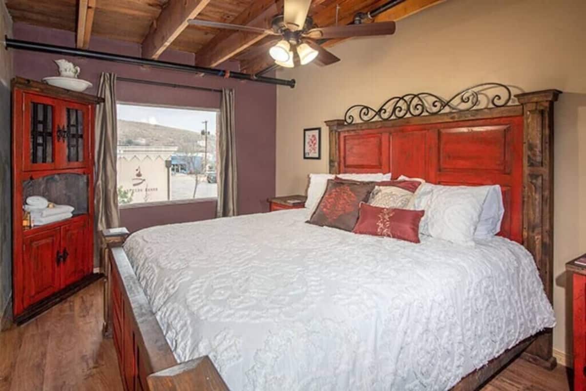 A bedroom with a large bed, wooden headboard, and a ceiling fan.