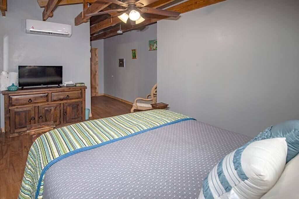 A bedroom with a bed, wooden dresser, television, and ceiling fan.