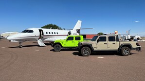 Un jet privato parcheggiato sul piazzale di sbarco, con un veicolo di servizio verde brillante e una persona in piedi accanto.