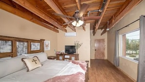 Una camera da letto con un letto grande, travi in legno a soffitto, una ventola a soffitto, televisore e una finestra con tende.