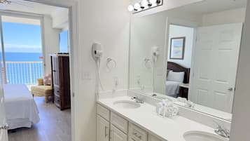 Een hotelbadkamer met twee wastafels, een grote spiegel en uitzicht op de oceaan door een deur.