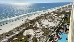 A beach resort with a long sandy beach, a wooden boardwalk, and a swimming pool.