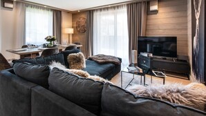 Un salon moderne avec un canapé foncé, un téléviseur à écran plat et un coin repas avec une table mise pour deux personnes.