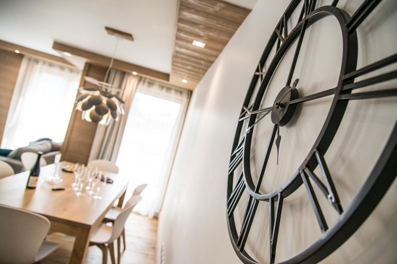 A modern dining area with a large wall clock, a wooden dining table, and a hanging light fixture.