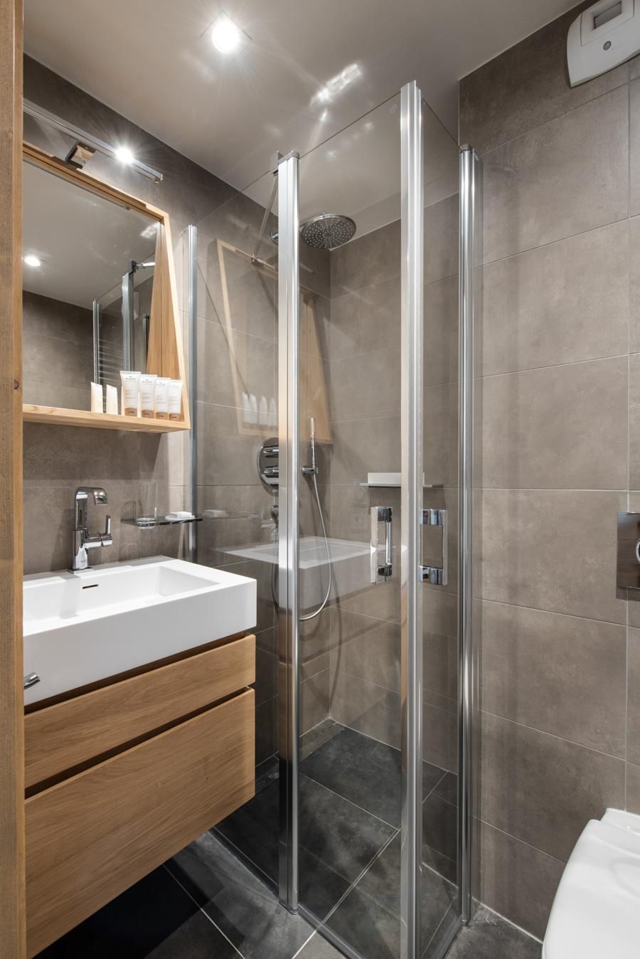 Un bagno moderno con doccia vetro, lavandino bianco e mobile bagno in legno.