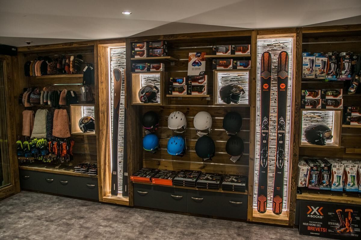 Un magasin d’articles de ski où l’on trouve des étagères remplies de casques, de lunettes de ski et de paires de skis.