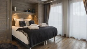 Een moderne slaapkamer met een houten hoofdbord, een groot bed met veel kussens en een nachtkastje.