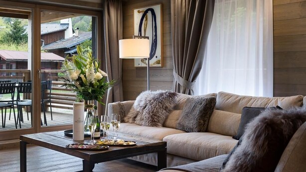 Een moderne woonkamer met een bank, een bijzettafeltje met bloemen en een uitzicht op de omgeving door grote ramen.