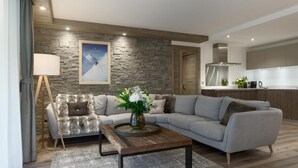 A modern living room with a stone accent wall, a grey sofa, a wooden coffee table, and a painting of a mountain scene. - Wifi, 200m from ski slopes, 1st floor, sauna, hammam, terrace, parking, tv, 81m², Les Gets (Les Gets)