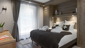 A modern hotel room with a large bed, a wooden headboard, a desk with a plant, and a window with curtains. - Wifi, 200m from ski slopes, 1st floor, sauna, hammam, terrace, parking, tv, 81m², Les Gets (Les Gets)