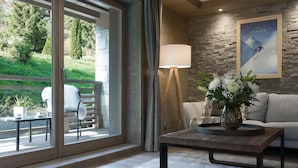 A modern living room with a sofa, a coffee table with a vase of flowers, a lamp, and a view of a garden through large sliding doors. - Wifi, 200m from ski slopes, 1st floor, sauna, hammam, terrace, parking, tv, 81m², Les Gets (Les Gets)