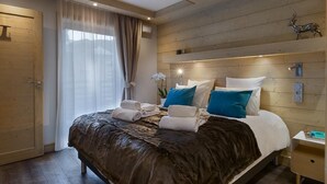 Un dormitorio bien iluminado con cabecera de madera, cama con cubierta marrón oscuro y una mesita de noche con lámpara.