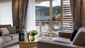 Una sala de estar moderna con un sofá, una mesa de centro con un jarrón de flores y vistas a un área boscosa a través de grandes ventanales.