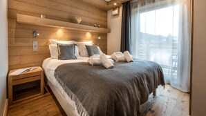 A modern hotel room with a wooden headboard, a large bed with grey bedding, a nightstand, and a view of a balcony. - Wifi, resort center, 1st floor, sauna, hammam, balcony, parking, tv, 82m², Les Gets (Les Gets)
