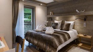 Een slaapkamer met een groot bed, een houten hoofdbord, een klein nachtkastje en uitzicht op groen.