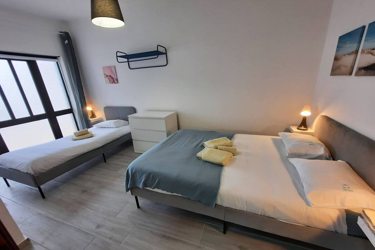A modern bedroom with two single beds, a bedside table, a nightstand, and a wall-mounted shelf.