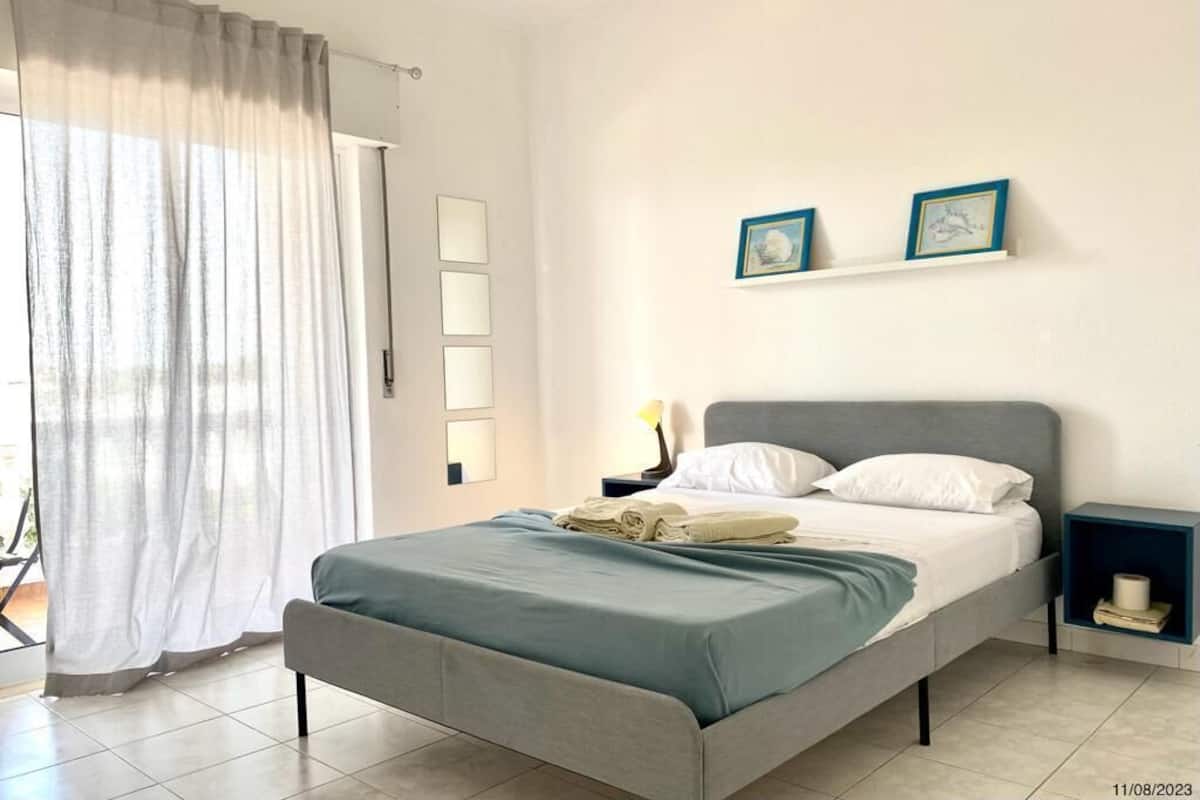 A bedroom with a bed, a nightstand, a lamp, and a window with curtains.