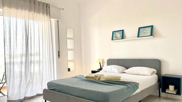 Un dormitorio con cama, mesita de noche, lámpara y ventana con cortinas.