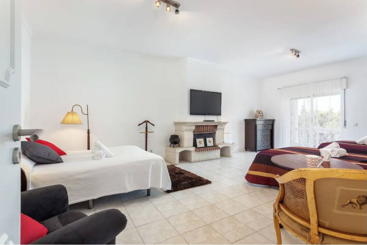 A modern hotel room with a bed, a sofa, a fireplace, a television, and a window with curtains.