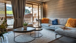 Een moderne woonkamer met een grijze bank, een rond bijzettafeltje en een groot raam met gordijnen.