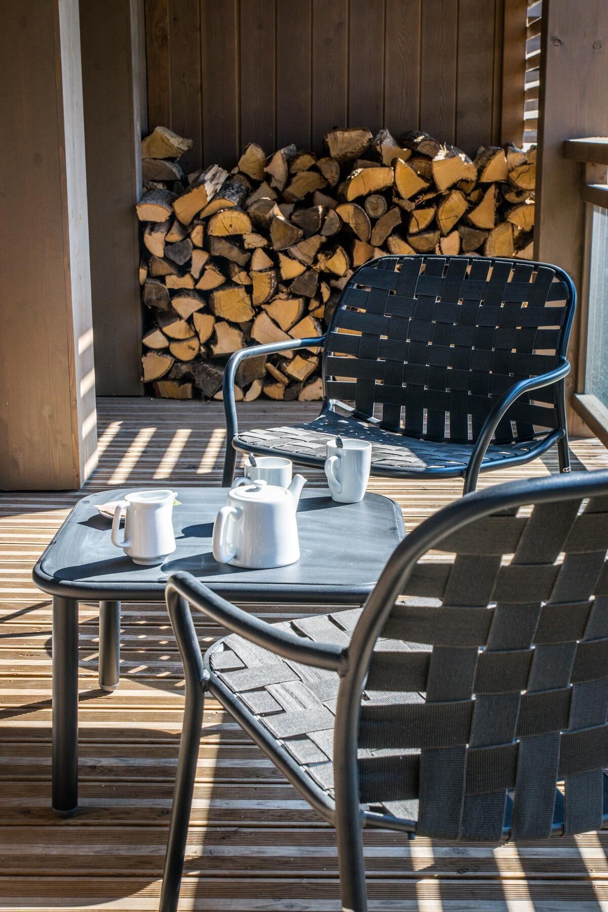 Un espace extérieur aménagé avec une table et des chaises, une pile de bois de chauffage en arrière-plan et une terrasse en bois.