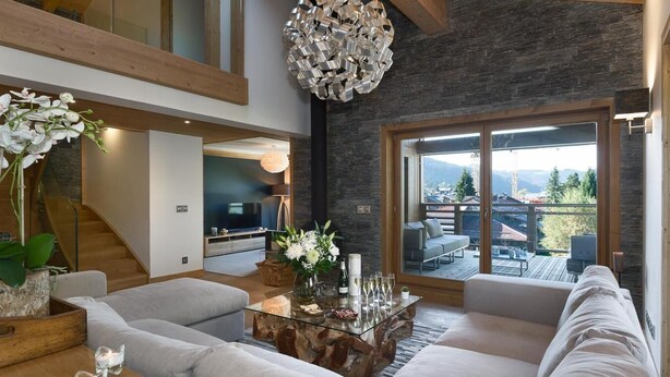 A modern living room with a large sofa, a glass coffee table, and a view of a balcony. - Wifi, 200m from ski slopes, 3rd floor, view village, sauna, hammam, balcony, fireplace or stove (Les Gets)