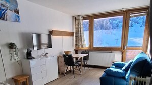 A modern bedroom with a bed, a desk, a chair, and a sofa. There is a window with a view of trees and a building. - Ski-in/ski-out & foot of the slopes, 6th floor, balcony, tv, 24m², La Plagne (La Plagne)